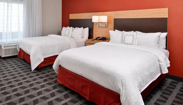The image shows a neatly arranged modern hotel room with two queen-sized beds with white and red bedding
