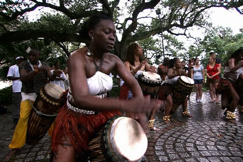 A group of people are playing African drums and dancing outdoors creating a vibrant and rhythmic cultural performance