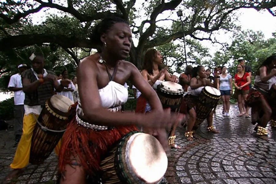 A group of people are playing African drums and dancing outdoors, creating a vibrant and rhythmic cultural performance.