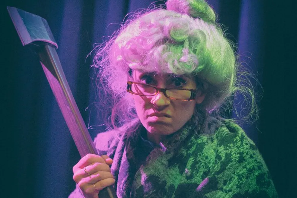 The image shows a person with a comedic expression wearing a green wig and glasses holding an axe which appears to be part of a costume or performance