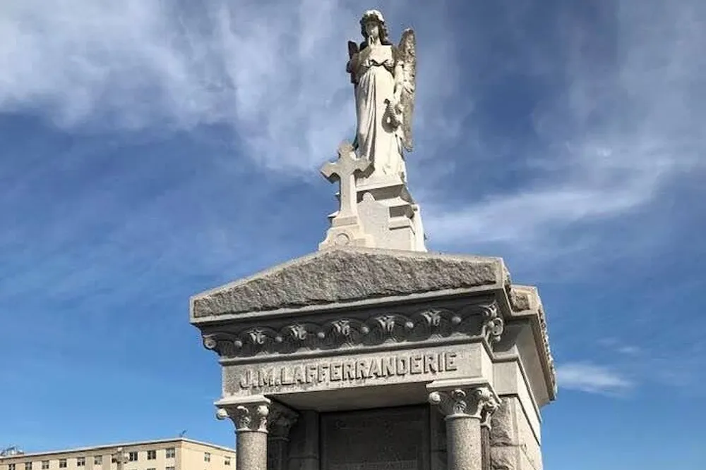 The image shows a sculpted angel atop a gravestone or monument under a blue sky