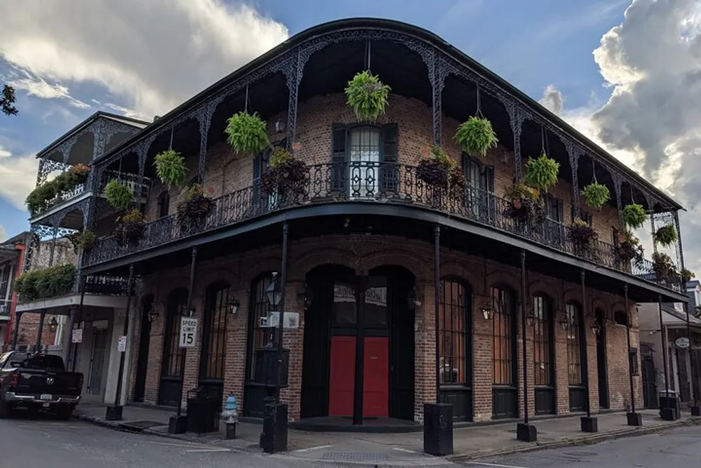 This image shows a two-story corner building with ornate iron balconies and hanging green plants characteristic of architectural styles commonly found in New Orleans French Quarter