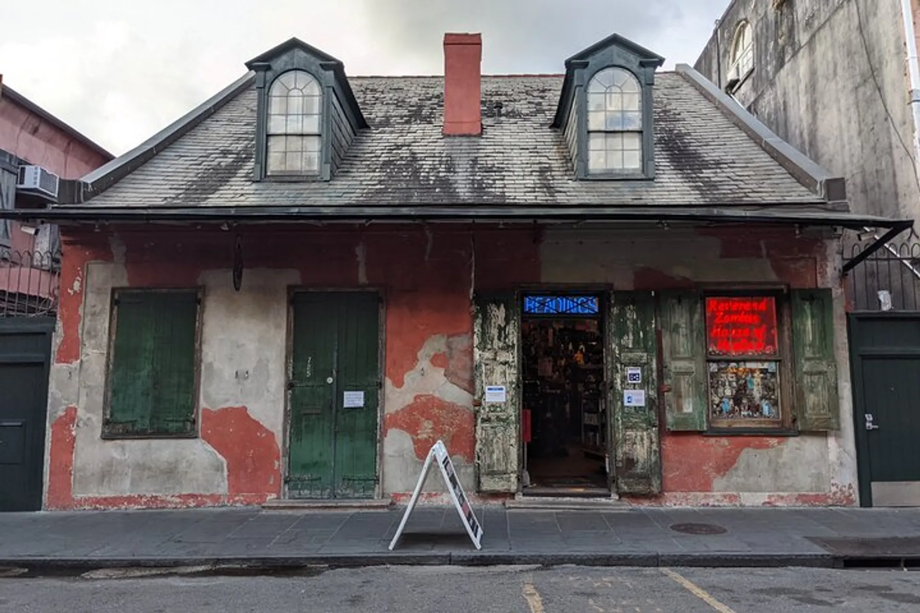 An old, weathered building with a peeling red facade, green shutters, and a sign offering readings, evoking a sense of history and mystery.