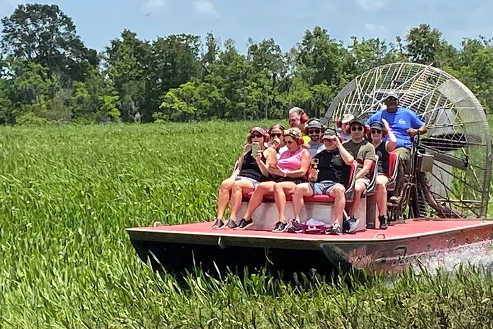 A group of people are seated on an airboat during a tour with greenery in the background and a clear blue sky above