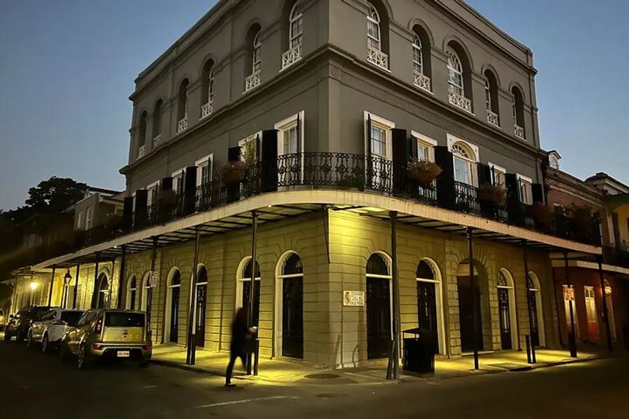 An atmospheric photo capturing an evening street scene with a historic building, featuring wrought-iron balconies and street lamps casting a warm glow.