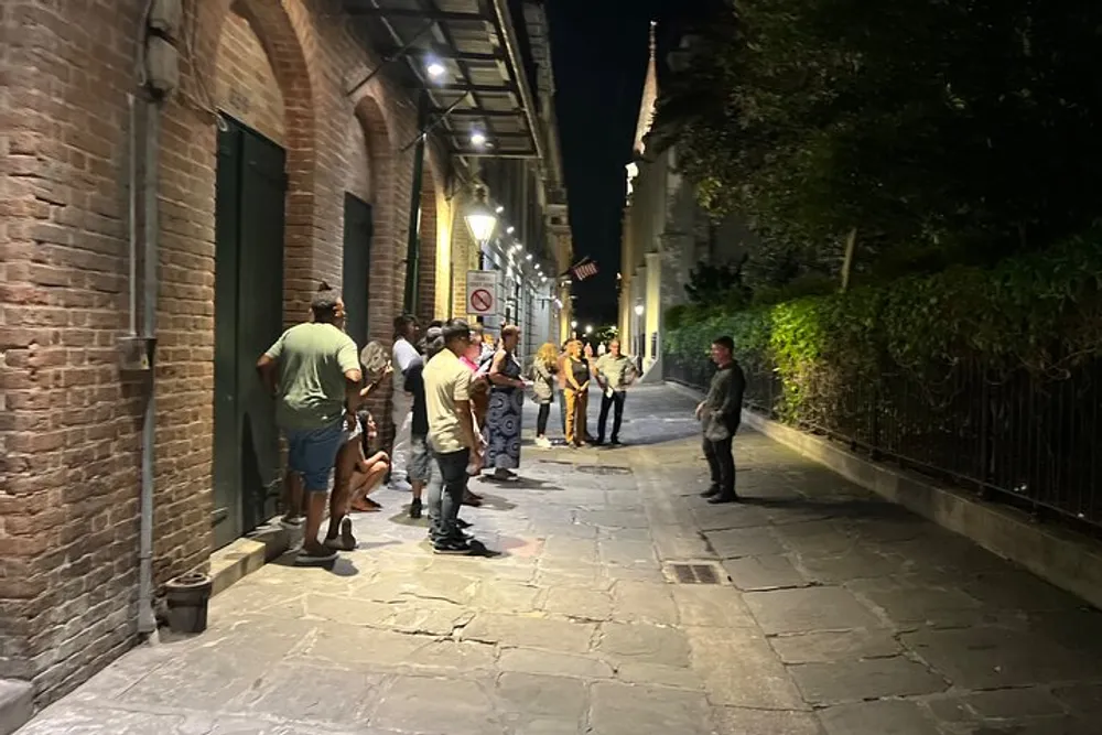 A group of people is standing and socializing on a well-lit narrow alleyway at night