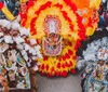 The image depicts individuals wearing vibrant and elaborate costumes featuring feathers and beadwork likely participating in a cultural or festival parade