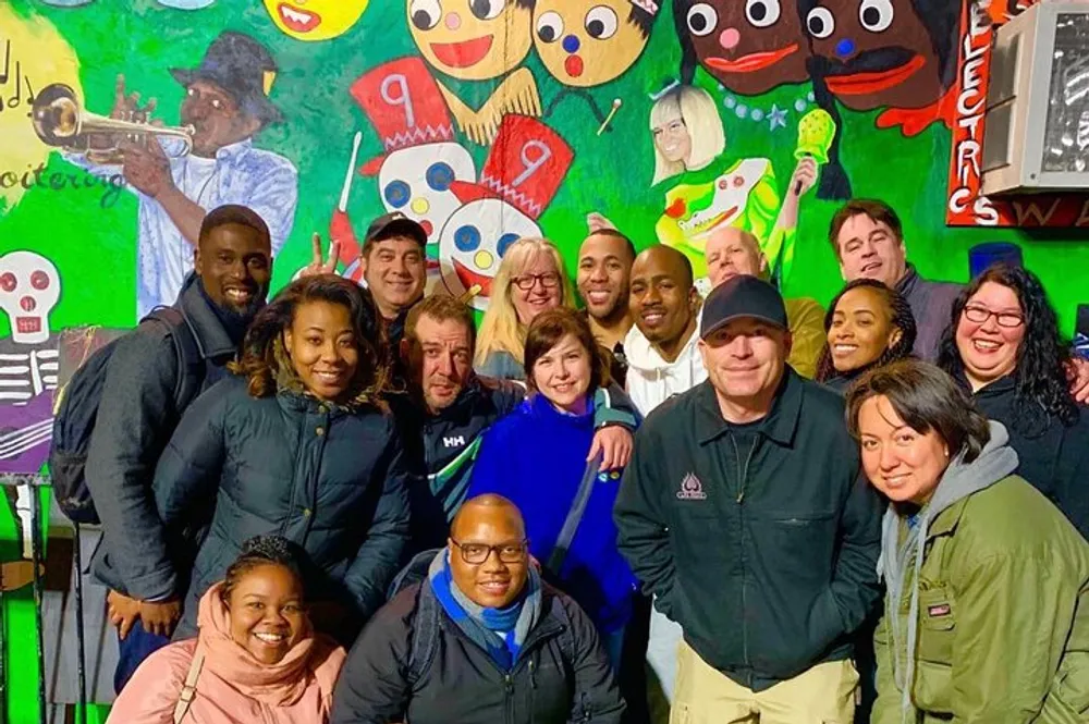 A diverse group of smiling people pose together in front of a colorful mural with a jazz and New Orleans theme