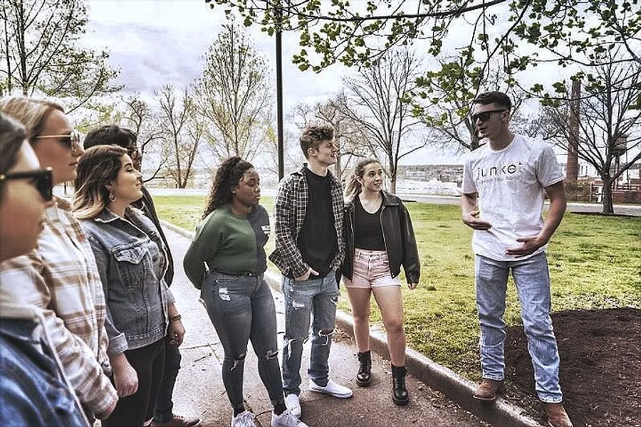 A group of young adults is engaged in a casual conversation in a park setting.