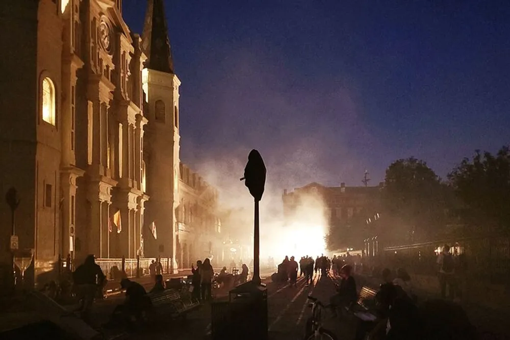 A dusky foggy scene outside a church with people milling about and streetlights casting a soft glow