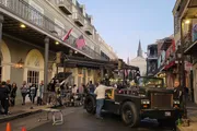 A film crew is busy setting up equipment for a shoot on a street lined with classic buildings, likely in the French Quarter of New Orleans.