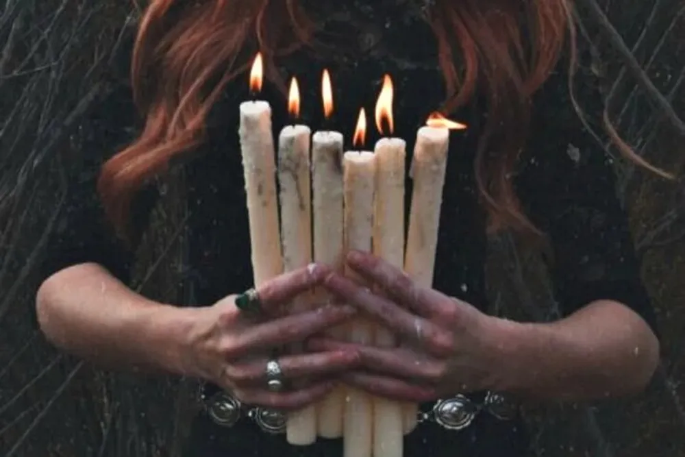 A person with red hair is holding several lit candles in their hands with snowflakes visible in the air around them