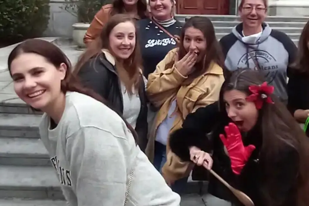 A group of people predominantly women are posing for a photo with varied expressions of happiness and surprise on their faces