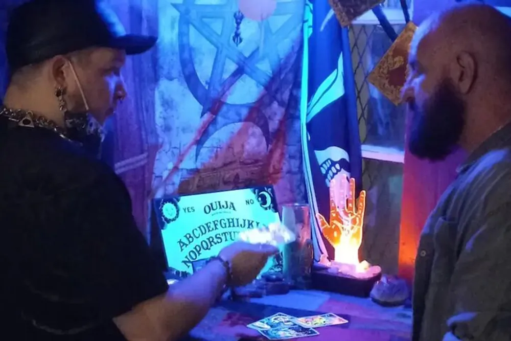A person appears to be giving a tarot reading or engaging in some kind of mystic ritual in a dimly lit room adorned with occult-themed decorations