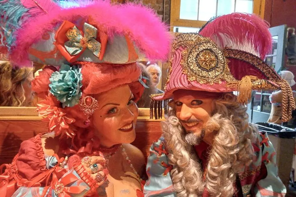 Two people are dressed in elaborate colorful costumes with fanciful hats likely at a festive event or celebration