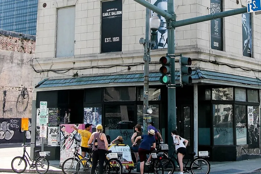 A group of cyclists is stopped at a city intersection in front of an old building with EAGLE SALOON EST 1851 signage