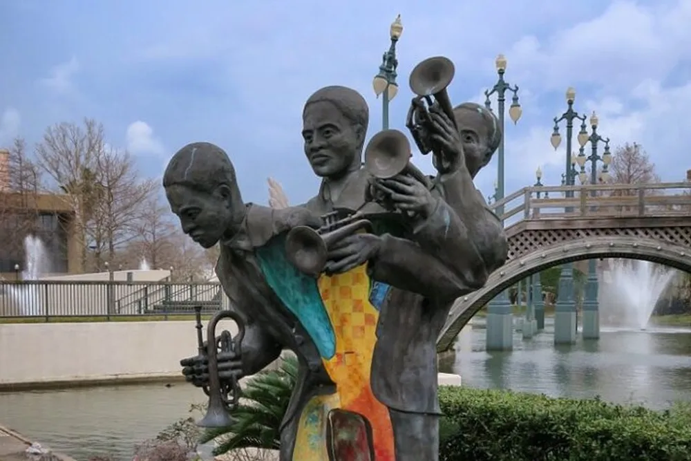 The image shows a sculpture of a jazz band with musicians playing brass instruments set against a backdrop of a bridge and water fountains