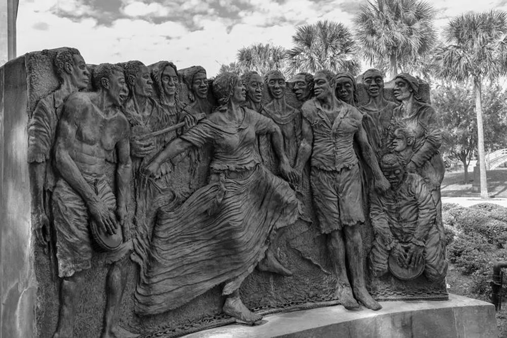 The image shows a black and white photograph of a detailed expressive sculpture depicting a group of figures possibly portraying a historical or significant cultural event