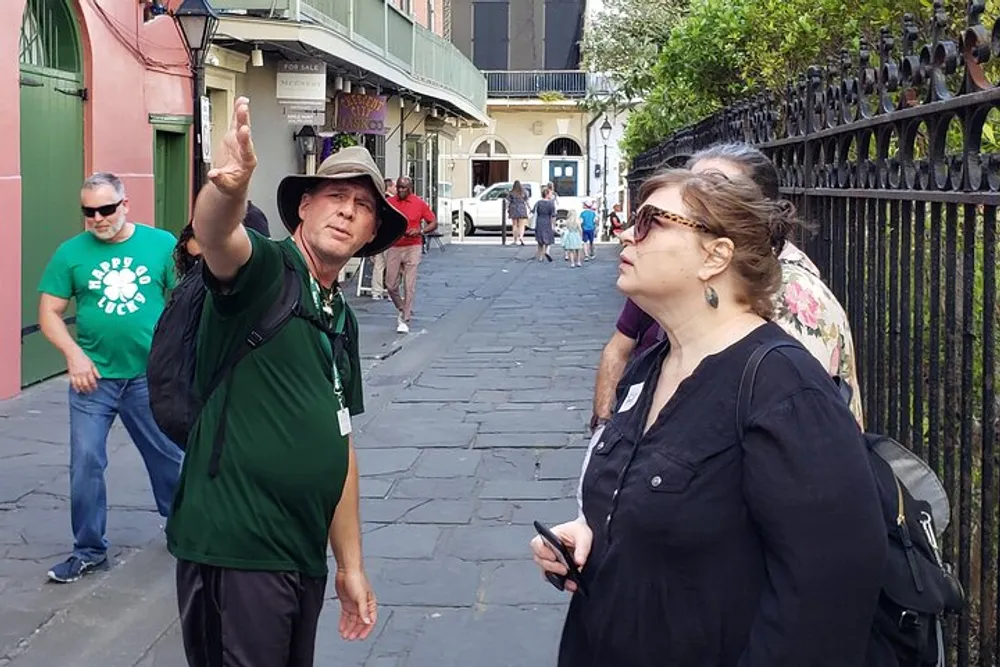 A tour guide is gesturing and explaining something to a woman on a city street possibly as part of a walking tour while other people walk by in the background