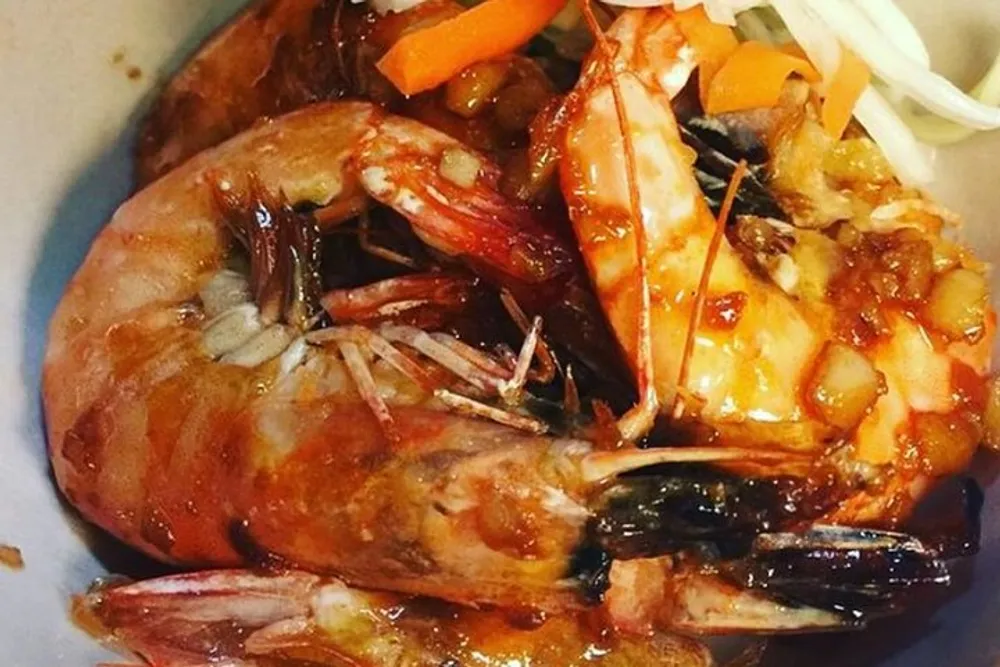 This image depicts a dish containing whole cooked prawns served with vegetables and a sauce