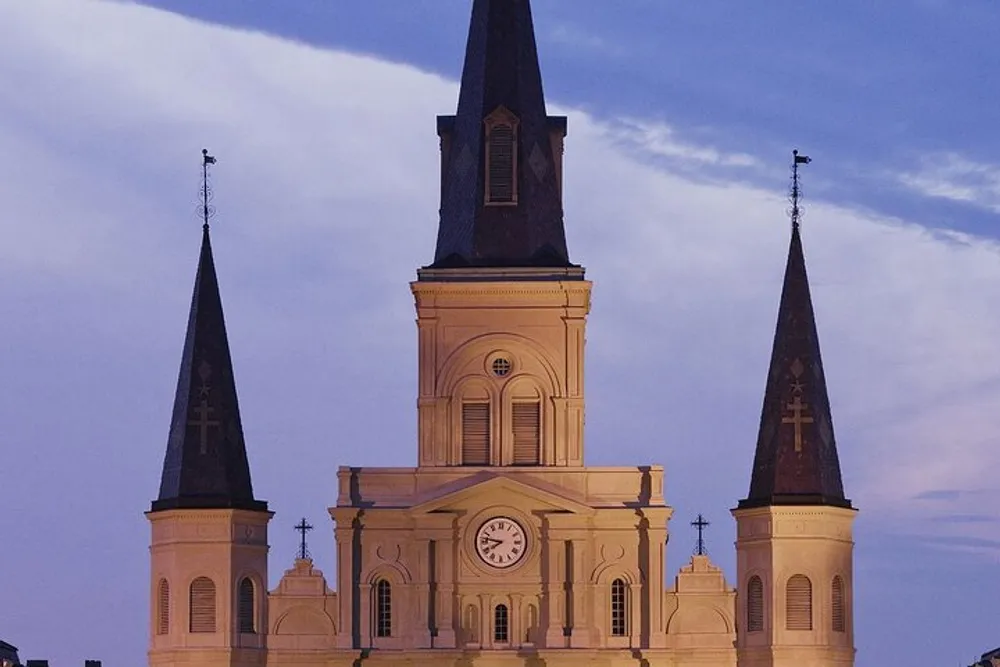 The image showcases the upper facade and the two towering steeples of a light-colored historic church against a twilight sky