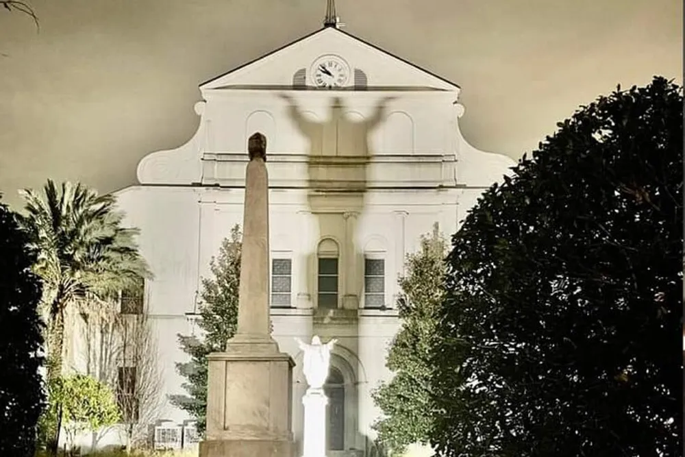The image shows a classic white building with a clock tower flanked by a tall monument and lush greenery captured in dim lighting that suggests dusk or dawn