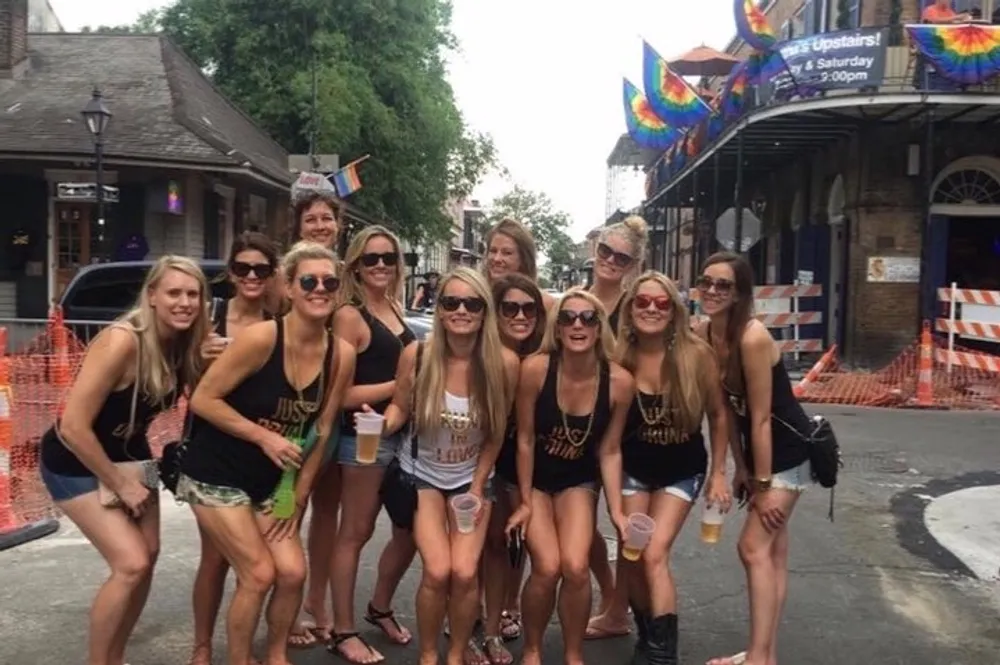 A group of women wearing matching tank tops are posing for a photo on a city street possibly celebrating a special occasion