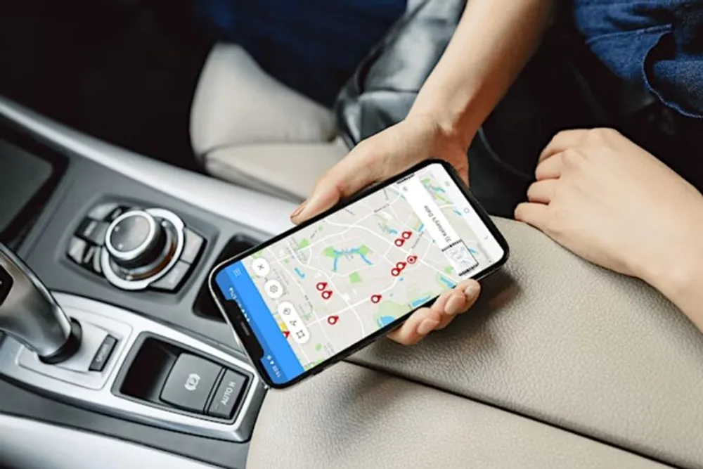 A person in a vehicle is holding a smartphone displaying a map application with navigation indications