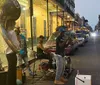 A trio of street musicians performs on a lively city street in the evening with one playing a tuba another on drums and a trumpet player all contributing to what appears to be a vibrant music scene