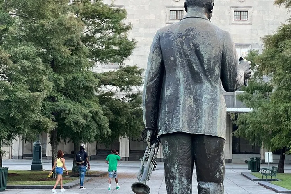A statue of a man holding a saxophone stands overlooking pedestrians in a tree-lined plaza