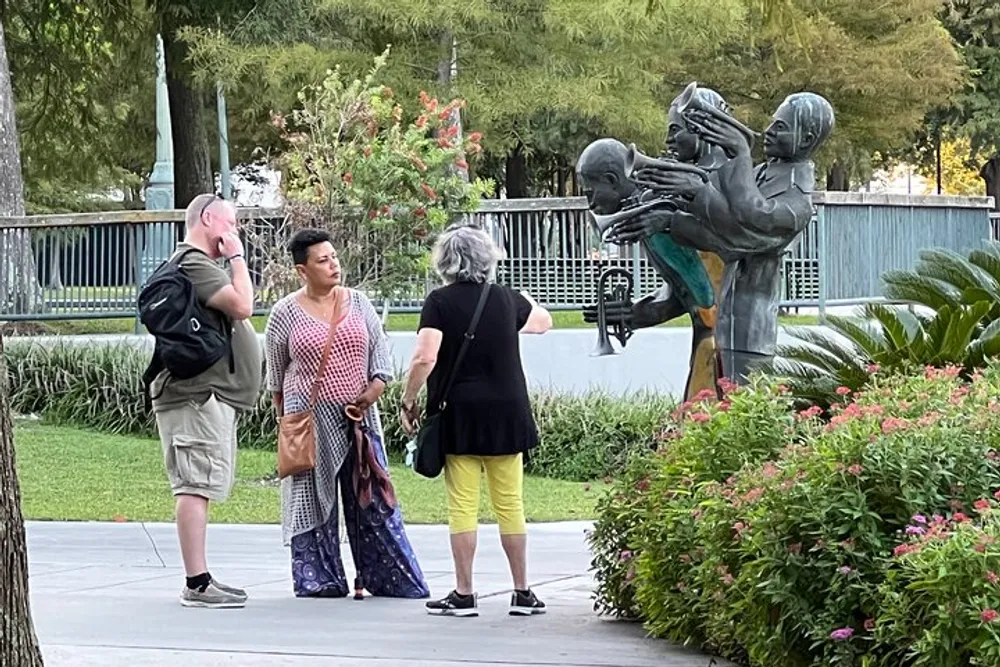 Three people appear to be engaged in conversation next to a statue of two figures in a park setting