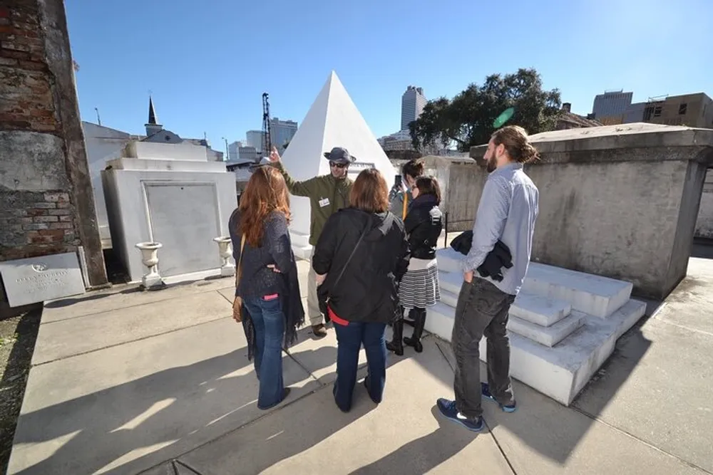 A group of people is attentively listening to a guide during a tour of a cemetery with distinctive above-ground tombs under a clear blue sky