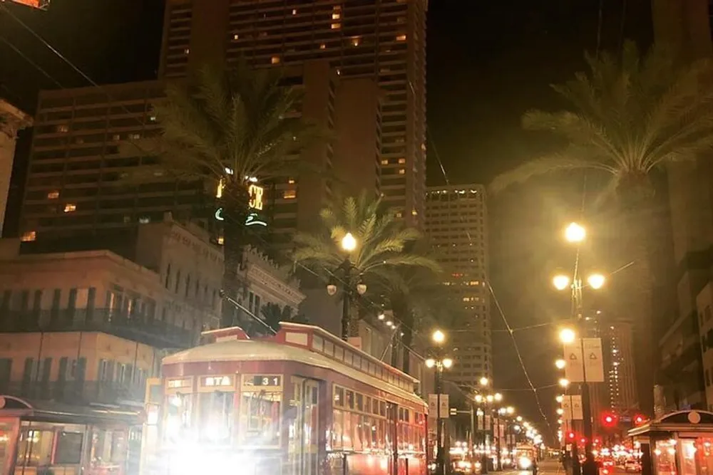 A streetcar travels through a palm-lined street at night amidst the illuminated cityscape