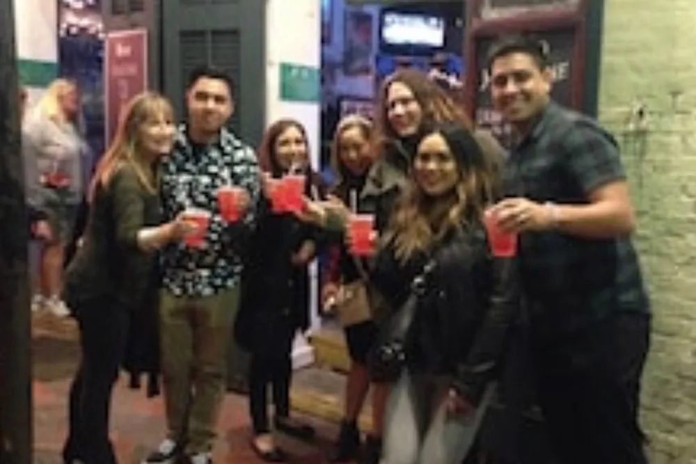 A group of people are smiling and holding up red cups in a casual outdoor setting possibly celebrating or enjoying a social event together