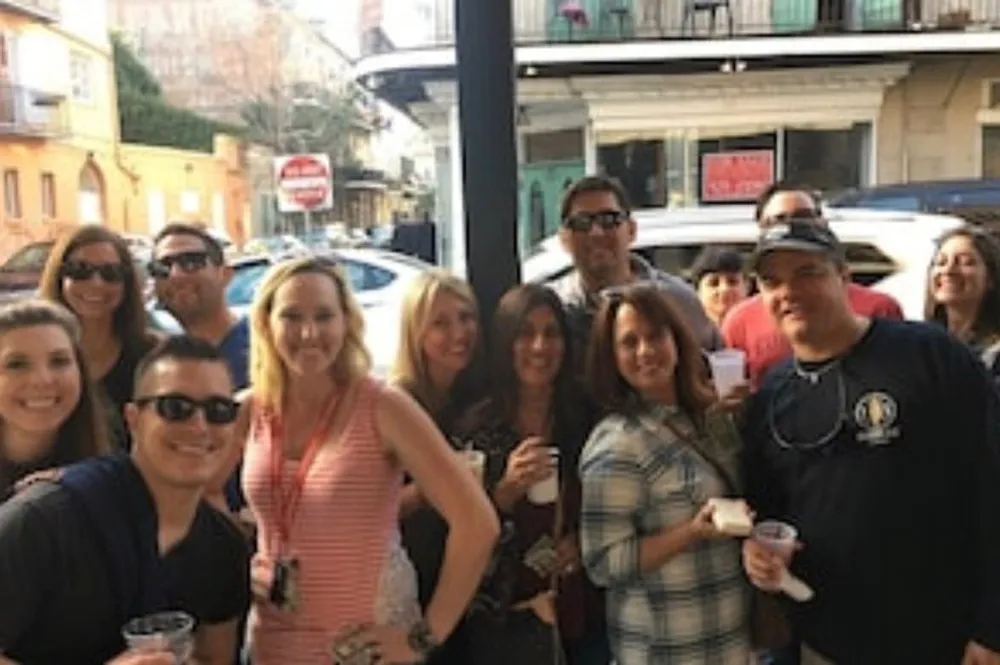 A group of people is smiling and posing for a photo on a busy street some holding drinks suggesting they might be out enjoying a social event together