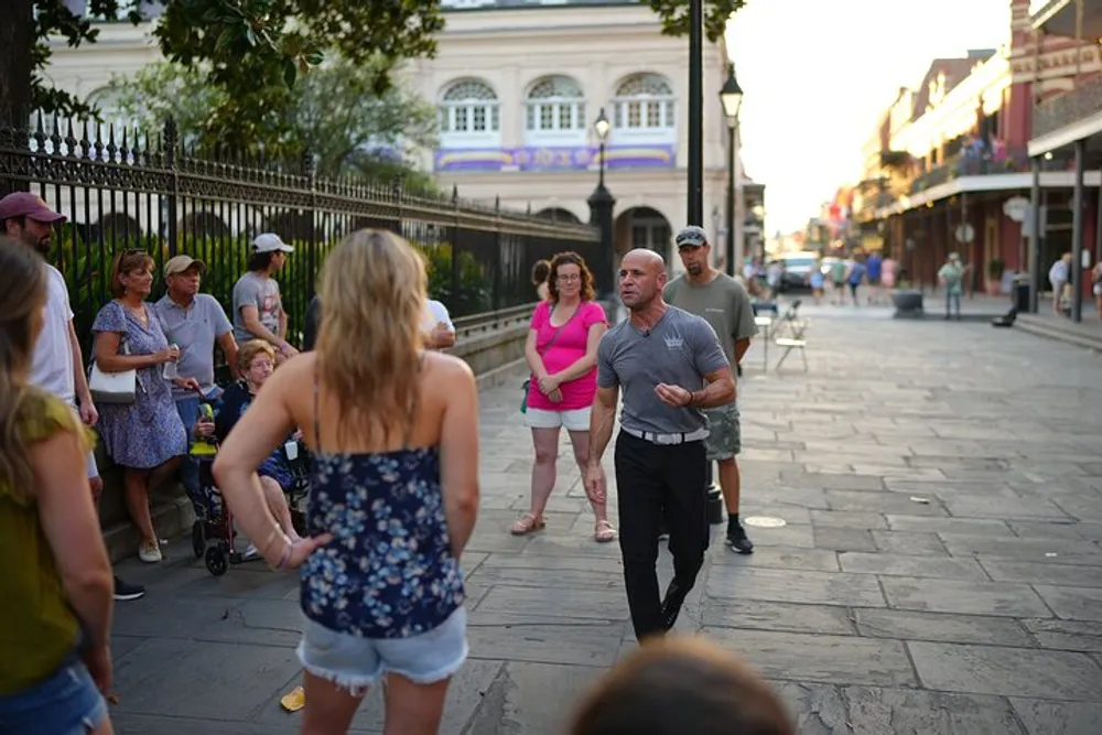A group of people gather on a street with one man in the center appearing to be speaking or performing to an attentive audience