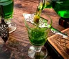 A green liquid likely absinthe is being poured into a glass over a slotted spoon with a sugar cube a traditional preparation method for this potent spirit