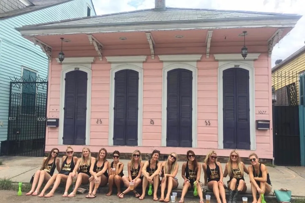 A group of people is posing in front of a pink house with blue shutters potentially during a social gathering or trip