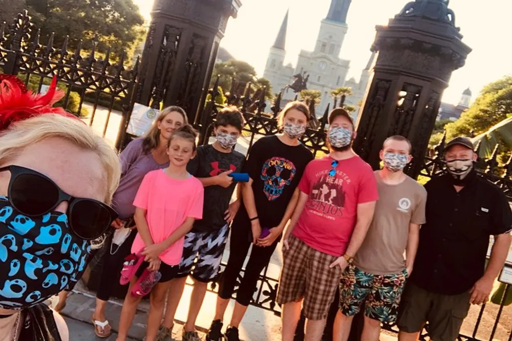 A group of people some wearing face masks take a selfie with a historical building in the background