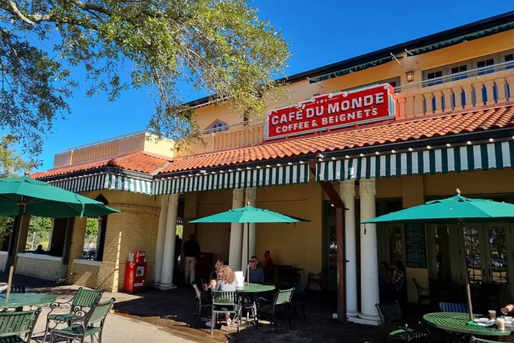 The image shows patrons sitting under green umbrellas at outdoor tables in front of the Caf du Monde a popular coffee stand known for its coffee and beignets