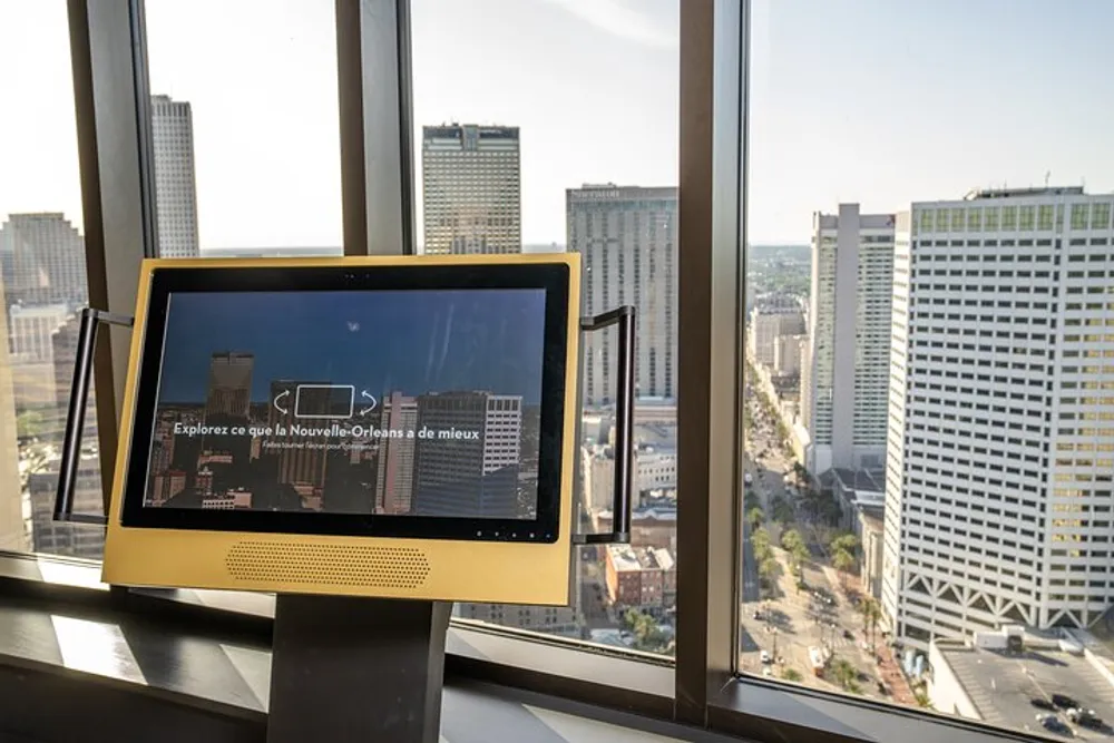 An interactive display possibly providing information about New Orleans overlooks a cityscape through large windows from a high vantage point