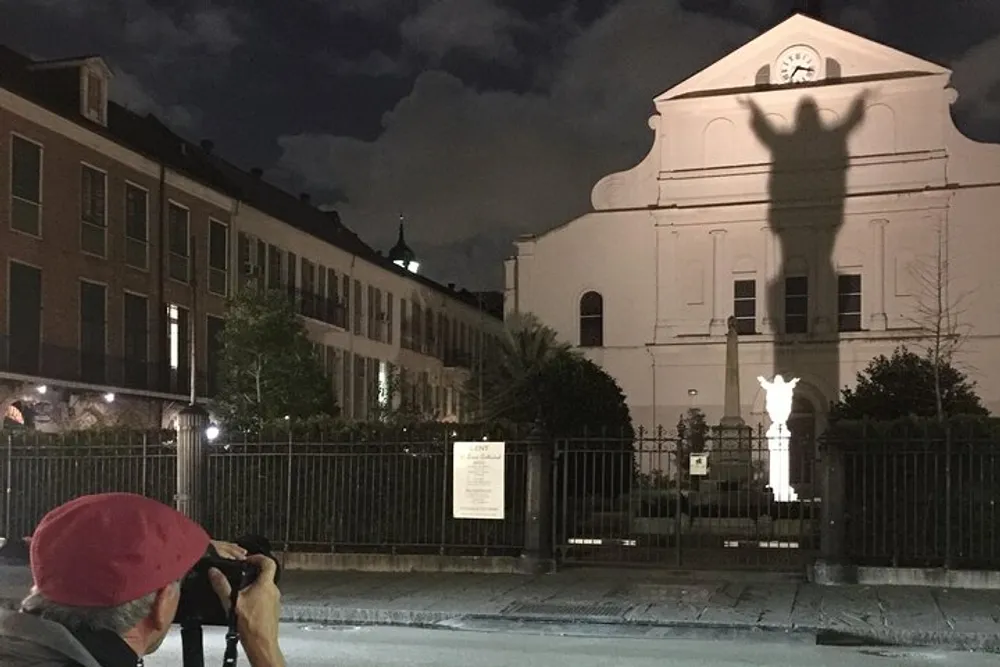 A person is photographing a building at night capturing an illuminated statues shadow cast on the facade