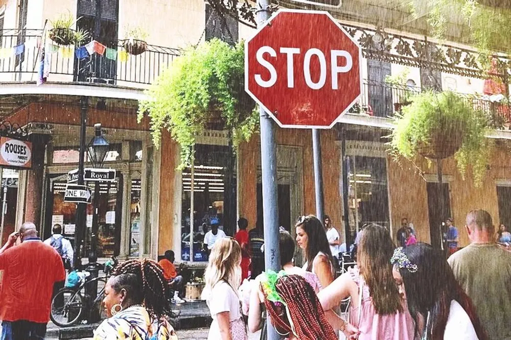 A diverse group of people is casually walking on a sunny street lined with shops and hanging plants with a prominent stop sign in the foreground