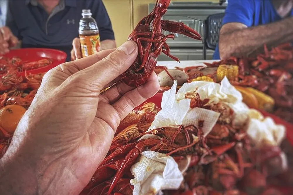 A person is holding a cooked crawfish over a table laden with more crawfish and fixings suggesting a communal seafood feast