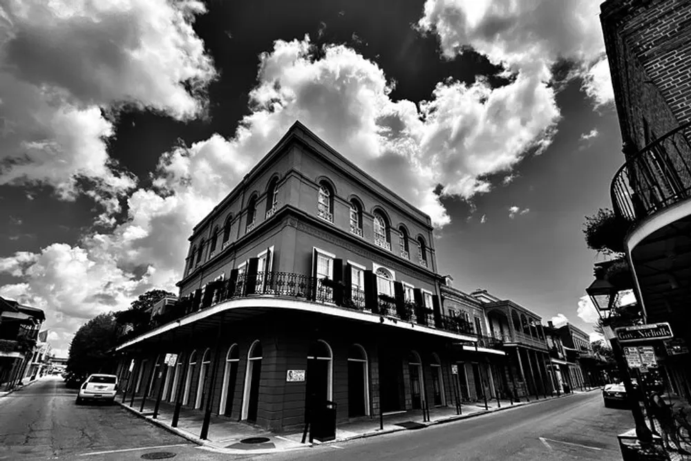 This is a black and white image depicting a historic corner building with balconies in what appears to be a quiet old-fashioned urban street under a cloudy sky