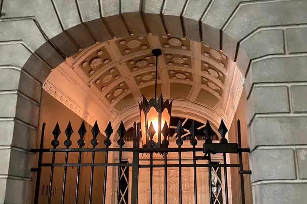 An ornate arched entrance with a geometric coffered ceiling is partially obscured by a decorative wrought iron gate topped with fleur-de-lis finials and an illuminated hanging lantern