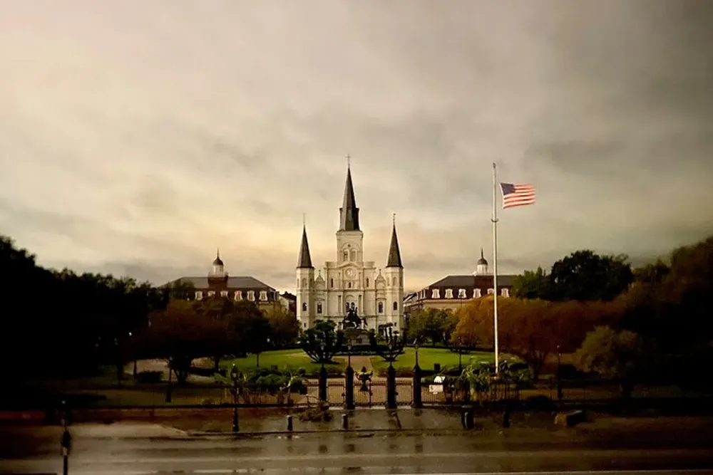 An overcast sky broods above the iconic St Louis Cathedral in New Orleans with the American flag flying at half-mast to the right likely signifying a period of mourning or remembrance