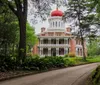 The image displays a grand historic mansion with a red-domed cupola surrounded by lush greenery under a partly cloudy sky