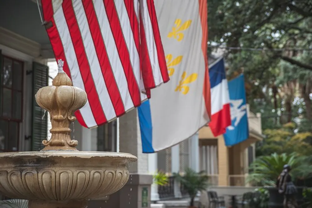 The image shows a water fountain in the foreground with various flags including an American flag hanging in the background in an urban setting suggesting a patriotic or ceremonial location