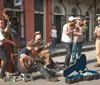 A group of street musicians is performing live on a city sidewalk playing an upright bass acoustic guitars and a violin with an open guitar case in front for tips